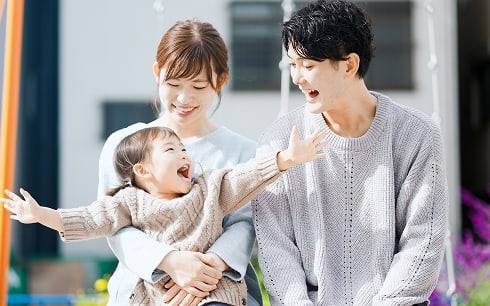 여성의 품에 안겨 남성을 향해 두 팔을 벌리며 웃는 아이